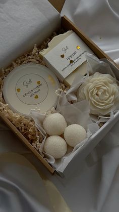 an open box with some flowers and soaps in it on a white bed sheet