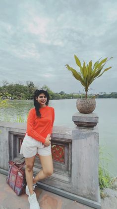 a woman standing next to a wall near a body of water with a plant in the background