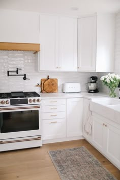 a kitchen with white cabinets and an oven in the center, along with a rug on the floor