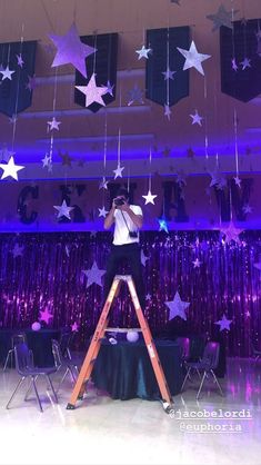 a man standing on a ladder in front of a stage with stars hanging from the ceiling