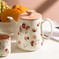 a tea pot and cup sitting on a table next to a bowl of oranges