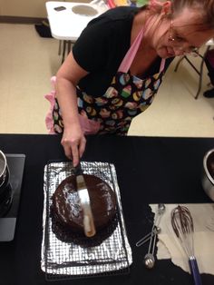 a woman is decorating a cake with chocolate icing on a black counter top