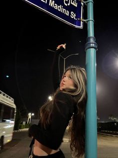 a woman leaning up against a street sign at night with her arm in the air