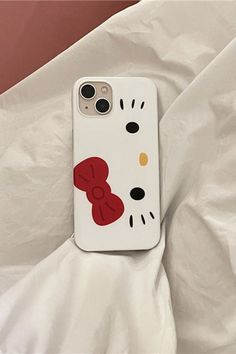 a hello kitty phone case laying on top of a white sheet with a red bow