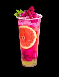 a glass filled with fruit and ice on top of a black table next to a slice of orange