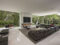 a large living room with couches and a fireplace in the center, surrounded by trees