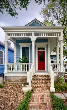 a small blue and white house with a red door on the front porch is shown