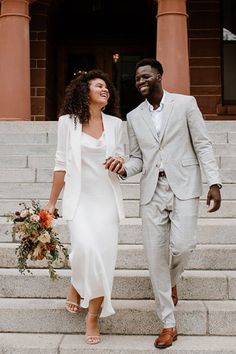 a man and woman are walking down the steps together in front of a building holding hands