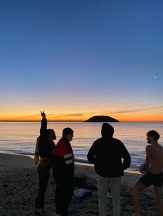 four people standing on the beach at sunset