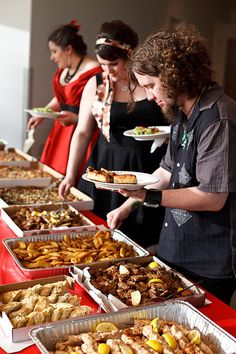 several people standing at a buffet line with plates of food on trays in front of them