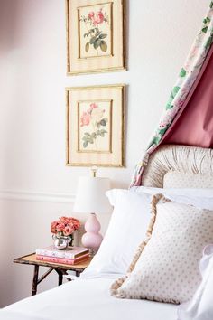 a bed with white sheets and pink flowers on the headboard next to two framed pictures