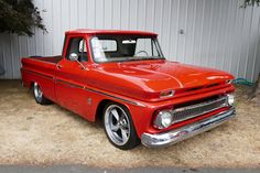 an old red pickup truck parked in front of a building with a white wall behind it