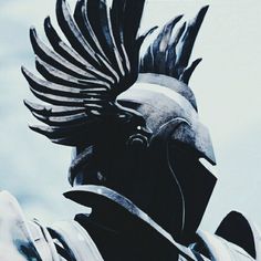 a black and white photo of a statue with feathers on it's head, in front of a blue sky