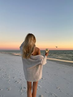 a woman is standing on the beach and holding a wine glass in her hand while looking out at the ocean