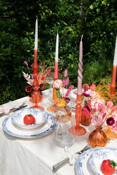 the table is set with plates, candles and strawberries on it for an elegant dinner