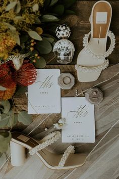 wedding stationery with shoes, rings and flowers on wooden table next to vases