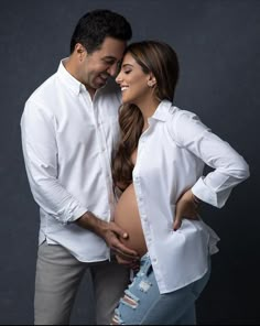 a man and woman standing next to each other in front of a dark background with their hands on the stomach