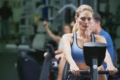 a woman on a stationary bike in a gym with other people behind her looking at the camera