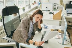 a woman is sitting at her desk in an office talking on the phone and looking at paperwork