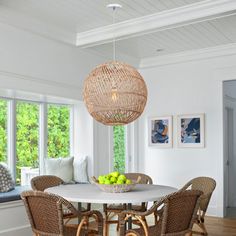 a dining room table with wicker chairs and a bowl of fruit on the table