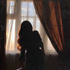 a woman standing in front of a window with the sun shining through her sheer curtains