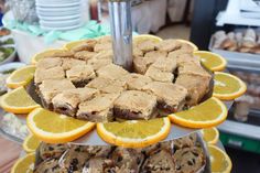 an assortment of desserts displayed on trays at a buffet or bakery shop with orange slices and brownies in the foreground