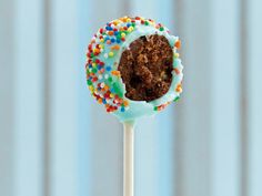 a cake pops with frosting and sprinkles on a white stick in front of a blue curtain