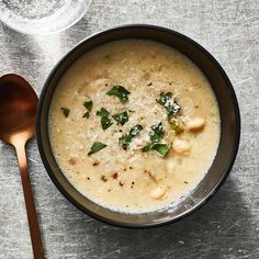 a black bowl filled with soup next to a spoon on top of a gray table