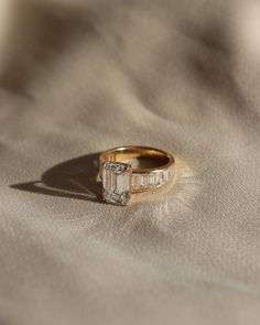 a gold ring with a baguette cut diamond in the center on a beige cloth