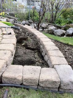 a brick wall in the middle of a garden area with grass and rocks around it