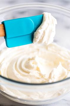 a blue spatula scooping cream into a glass bowl