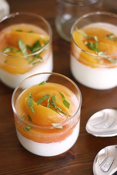 three desserts in small glass dishes on a wooden table with spoons and utensils