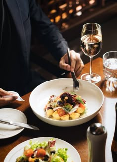 a person is cutting into a salad with a fork and glass of wine in the background