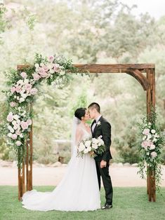 a bride and groom kissing under an arch with flowers