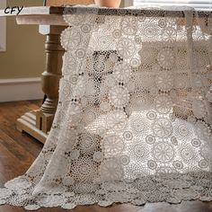 a white crocheted table cloth on top of a wooden table next to a window