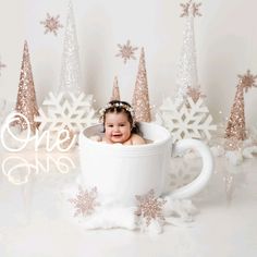 a baby is sitting in a coffee cup surrounded by snowflakes and christmas trees