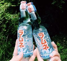 two bottles of soda are held up in front of some trees