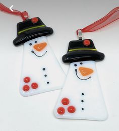 two snowmen wearing hats and scarfs are hanging from red ribbon on white surface