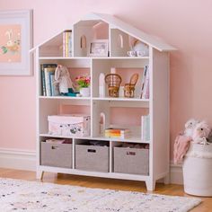 a white bookcase with baskets and toys in it next to a pink painted wall