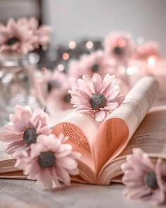 an open book sitting on top of a table with pink flowers in front of it