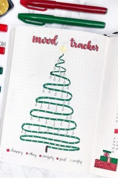 a christmas tree drawn on a notebook surrounded by markers and crayon pencils