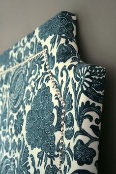 a blue and white wall hanging with beads on it's side, next to a gray wall