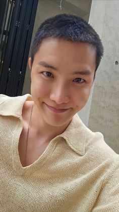 a young man is smiling at the camera with his hand on his hip and wearing a tan sweater