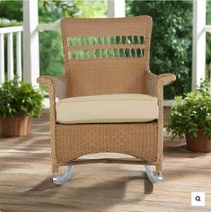 a wicker rocking chair on a deck with potted plants in the back ground