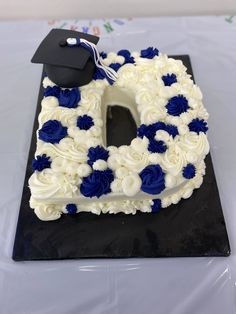 a cake with white frosting and blue flowers in the shape of a letter shaped like a graduation cap