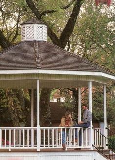 a white gazebo sitting on top of a lush green park covered in trees and grass