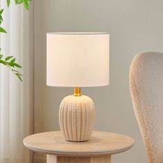 a white table lamp sitting on top of a wooden table next to a white chair