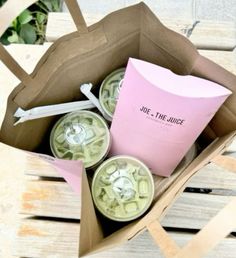 some drinks are sitting in a box on a wooden table and one is pink, the other is green