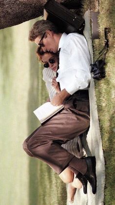 a man and woman leaning against a tree with their arms around each other while reading