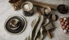 an assortment of kitchen utensils and ingredients on a marble counter top with eggs in bowls